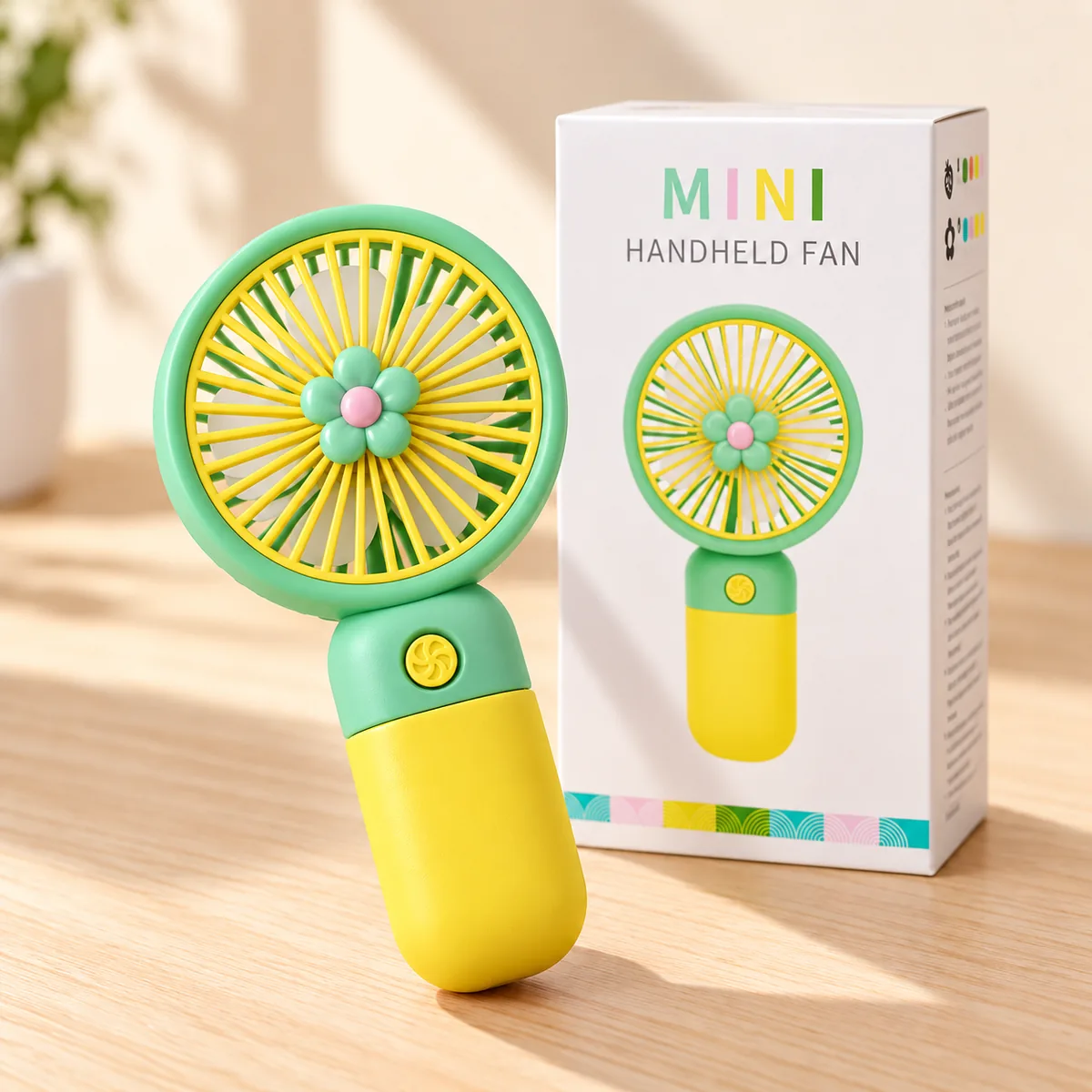 A mint-and-yellow flower fan standing beside its printed Mini Handheld Fan gift box