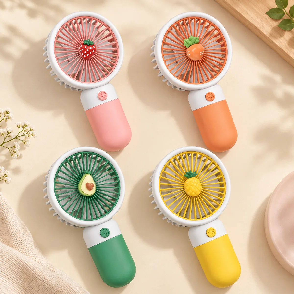 Four fruit-design mini fans laid out — strawberry, carrot, avocado and pineapple charms on pink, orange, green and yellow handles