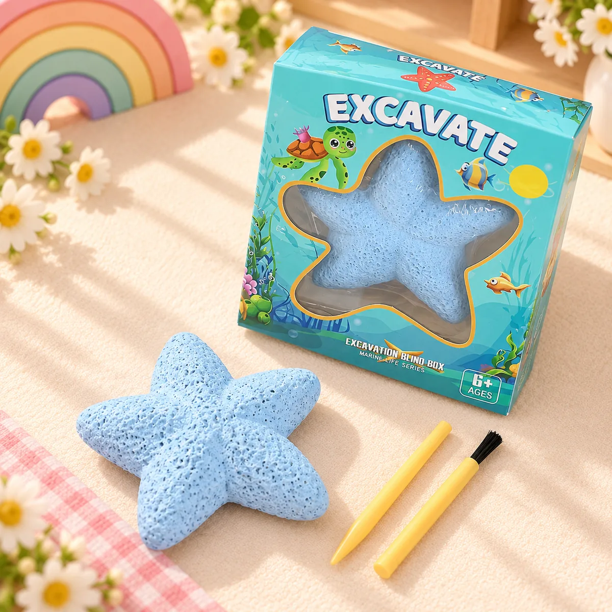 The Ocean Dig Kit box beside the blue starfish-shaped plaster block and the two yellow tools that come with it