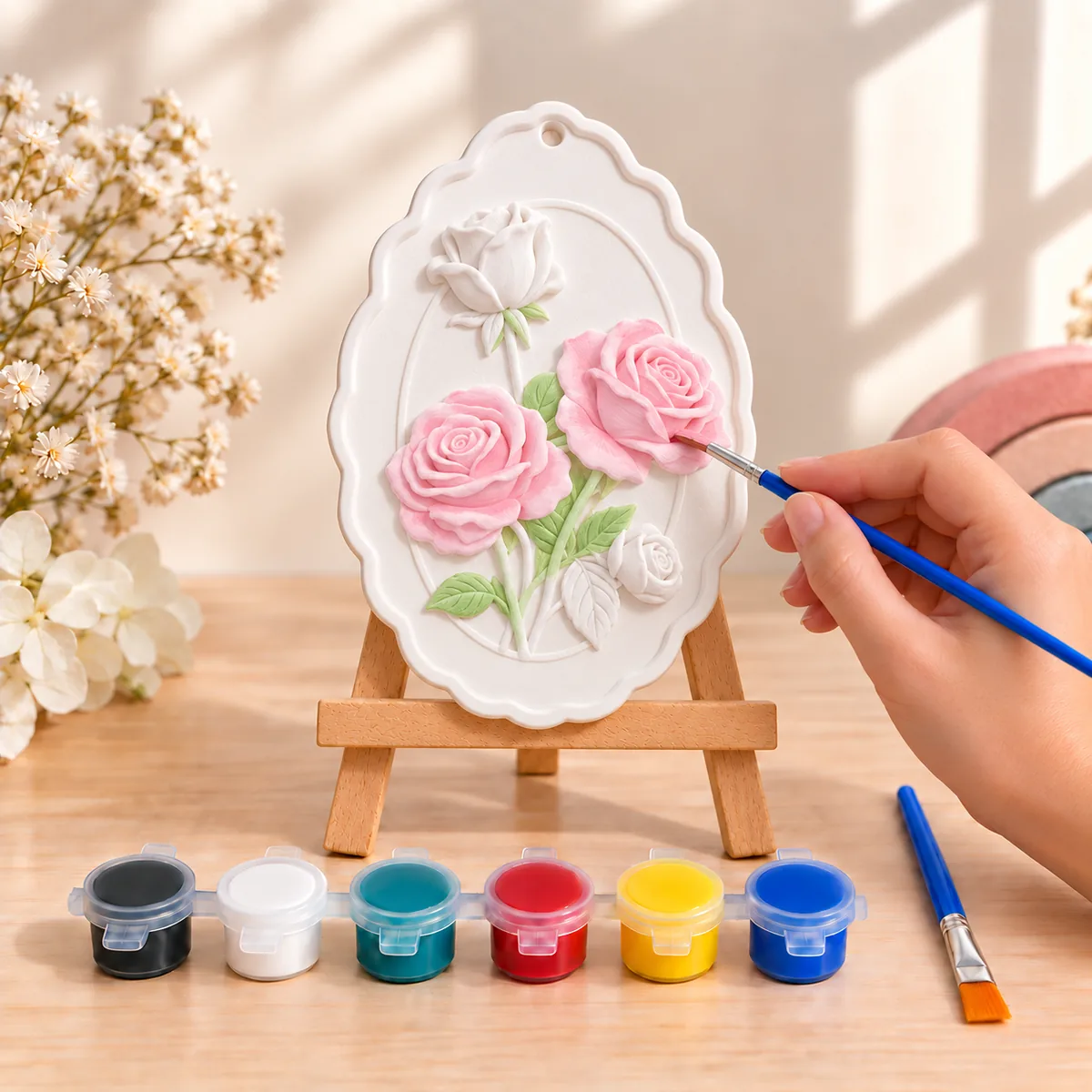 A rose plaque on a mini easel, two blooms painted soft pink with green leaves and two roses still bare white