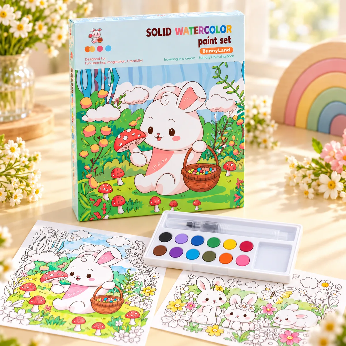 The BunnyLand book standing upright beside the open paint tray, water brush and two part-painted bunny scenes